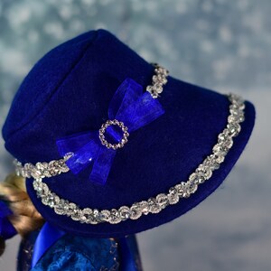 May include: A blue felt hat with a silver sequined trim and a blue satin bow with a rhinestone embellishment.