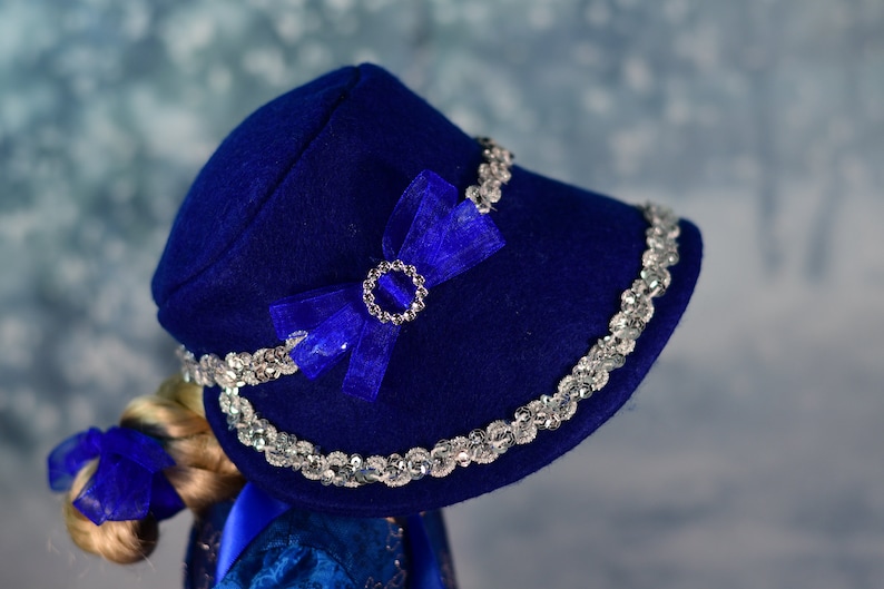 May include: A blue felt hat with a silver sequined trim and a blue satin bow with a rhinestone embellishment.