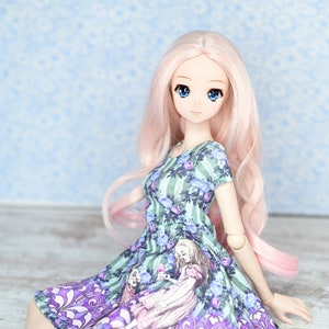 May include: A doll with long pink hair wearing a green and purple dress with a floral pattern. The dress features a print of a girl in a pink dress.