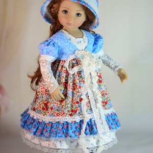 K&ouml;nnte beinhalten: Puppe in einem Kleid mit Blumenmuster, blauem Oberteil und passendem Hut. Das Kleid hat eine wei&szlig;e Spitzenborte und der Hut ist mit Blumen verziert. Die Puppe tr&auml;gt schwarze Schuhe.