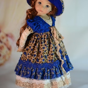 K&ouml;nnte beinhalten: Eine Puppe mit einem blauen Hut, der mit Stoffblumen verziert ist, und einem passenden Kleid. Das Kleid hat ein Blumenmuster mit blauen Akzenten, Spitzenbesatz und einem ger&uuml;schten Rock. Die Puppe hat lange, rotbraune Haare und tr&auml;gt schwarze Schuhe.