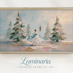 May include: An oil painting in a gold frame depicting a figure in a white dress holding a nutcracker amidst snow-covered pine trees. Below the frame, the text reads Luminaria PREMIUM FRAME TV ART in a blue script and serif font.