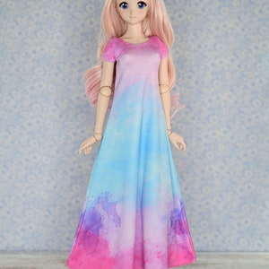 May include: A doll wearing a long, pink and blue tie-dye dress with short sleeves. The doll has long, pink hair and blue eyes. The doll is wearing blue shoes with white flowers.
