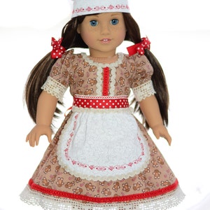 May include: A doll wearing a white chef hat, a brown dress with gingerbread men and candy canes, a red and white polka dot ribbon, and a white apron with red embroidery. The doll has brown hair in pigtails with red polka dot bows.