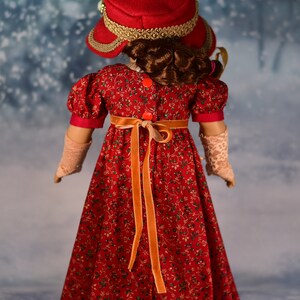 May include: A red dress with a floral pattern and a matching red hat with gold trim. The dress has a long orange ribbon tied at the waist.