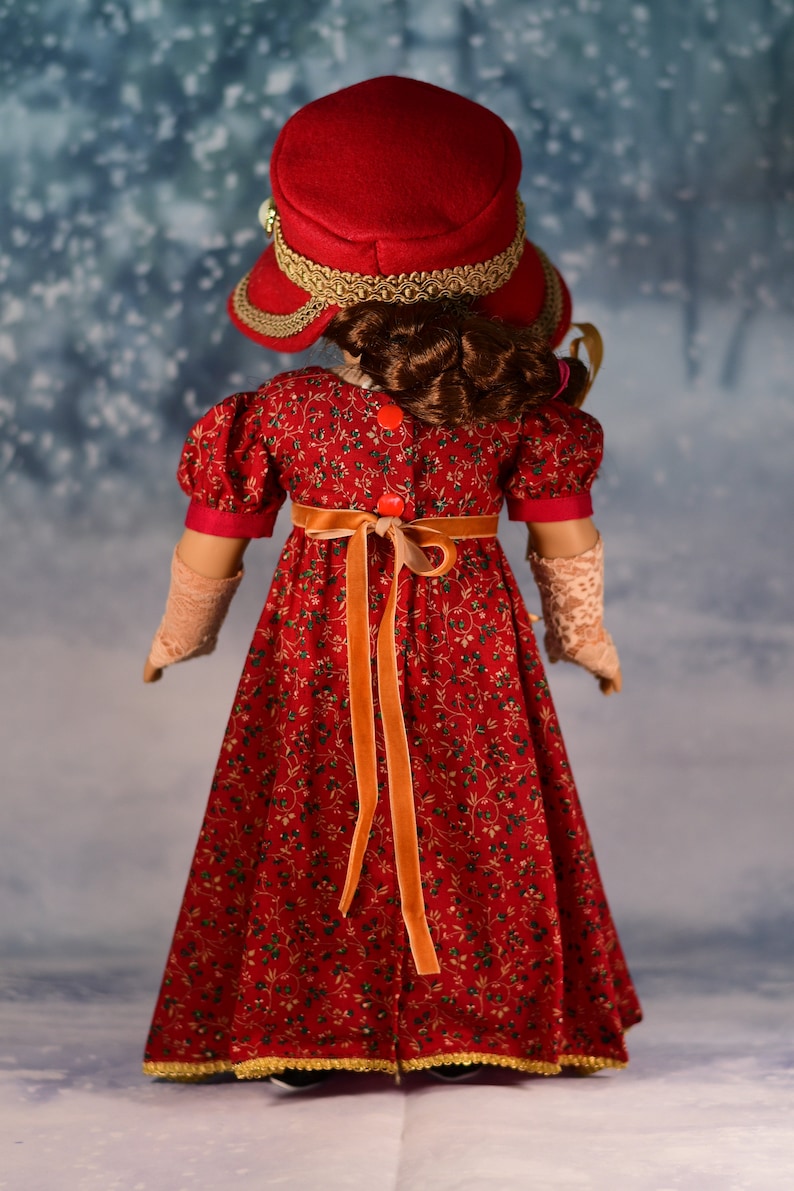 May include: A red dress with a floral pattern and a matching red hat with gold trim. The dress has a long orange ribbon tied at the waist.