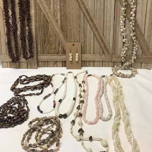 May include: A collection of 10 necklaces made of various materials, including shells, beads, and wood. The necklaces are displayed on a wooden background. There are also a pair of shell earrings.