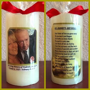 May include: A white candle with a red ribbon and a photo of a couple on the front. The candle has a gold label with the text "HIS JOURNEY'S JUST BEGUN" and a poem about remembering a loved one. The text on the bottom of the candle reads "In Loving Memory of Frederick Commay Jr. October 6, 1928 - February 26, 2017."