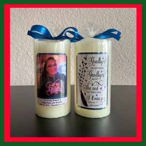May include: Two ivory-colored pillar candles with blue ribbon. One candle features a photo and text: "In Loving Memory of Angel Baby Girl Manyns June 14, 1978 - December 10, 2021." The other candle has text: "Goodbyes are not forever... I'll miss you."