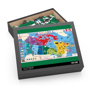 Puede incluir: Una caja de rompecabezas gris con un mapa colorido de Canadá en la tapa. El mapa muestra provincias y territorios con sus nombres. La caja dice "11x14 Puzzle 252 pcs Ages 9+". La caja está abierta, revelando piezas de rompecabezas.