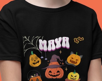 Może przedstawiać: Czarny T-shirt z motywem Halloween z imieniem "Maya" w retro czcionce. Projekt zawiera różne dynie z różnymi wyrażeniami, kapelusz czarownicy, nietoperze i gwiazdy.