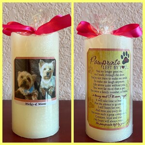 May include: A white pillar candle with a photo of two Yorkshire Terriers and the text "Mickey & Minnie". The candle has a pink ribbon tied around it and a label with the text "Pawprints Left By You..." and a poem about the loss of a pet.