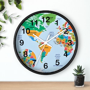 May include: A round wall clock with a black frame featuring a colourful world map on its face. The clock has white hour, minute, and second hands, and large black numbers from 1 to 12 positioned over the continents and oceans of the map.