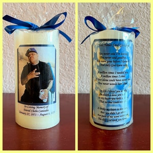 May include: Two white memorial candles with a blue ribbon. One candle has a photo of a man with a blue baseball cap and a can of beer in his hand. The other candle has a poem that reads "You Never Said Goodbye".
