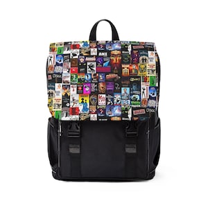 Peut inclure: Sac à dos noir avec fermeture à rabat et poignée supérieure. Le rabat supérieur est recouvert d'un collage d'affiches de comédies musicales colorées. La partie inférieure du sac à dos est noire unie avec deux poches latérales.
