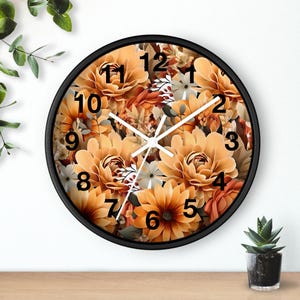 Puede incluir: Un reloj de pared redondo con marco negro. La esfera del reloj está llena de un diseño floral en tonos naranja, amarillo y blanco. Las manecillas son blancas y los números negros.