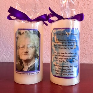 May include: Two white pillar candles with purple ribbons. One candle has a photo of a woman with glasses and the text "In Loving Memory of Kathy Moget". The other candle has a poem that reads "If Roses Grow In Heaven, If Roses grow in Heaven, Lord please pick a bunch for me, Place them in my Mother's arms and tell her they're from me. Tell her I love her and miss her and when she turns to smile, place a kiss upon her cheek and hold her for a while. Because remembering her is easy I do it every day, but there's an ache within my heart that will never go away."