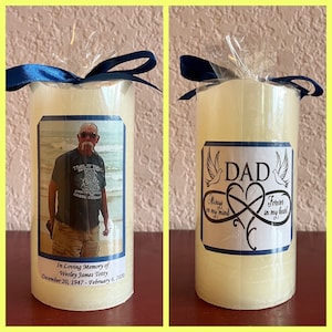 May include: A white pillar candle with a blue ribbon and a label that reads "In Loving Memory of Wesley James Totty December 20, 1947 - February 6, 2020" and a photo of a man in a "Trail of Tears" t-shirt. The candle is next to a white pillar candle with a blue ribbon and a label that reads "DAD" with doves and an infinity symbol with the text "Always in my mind" and "Forever in my heart".