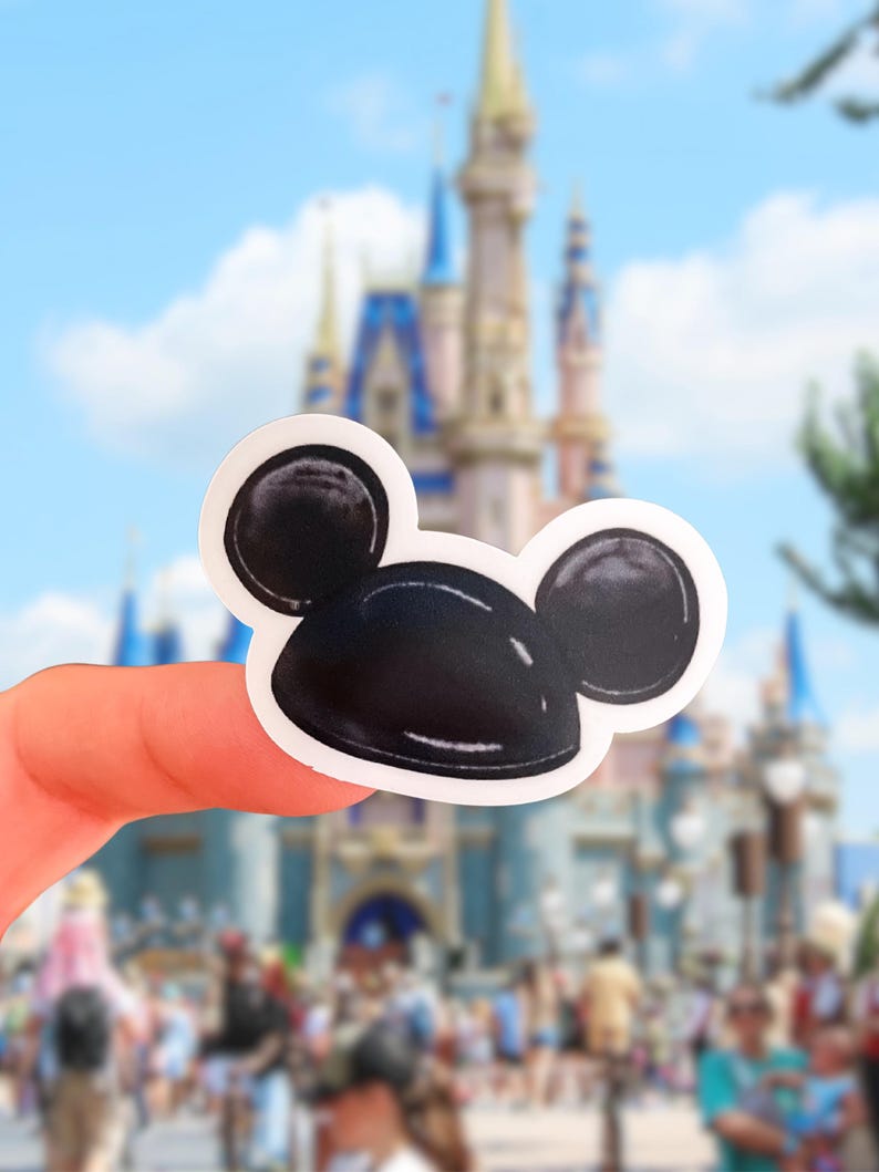 May include: A die-cut sticker featuring a glossy black Mickey Mouse ear hat with a white border. The design is a stylized illustration of the iconic headwear with rounded ears and a smooth, reflective surface, presented as a single adhesive decal.