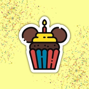 Op de afbeelding: Een sticker van een chocoladecupcake met gele glazuur, twee ronde bruine oren en een brandend kaarsje bovenop. Het cupcakevormpje heeft afwisselend blauwe en rode verticale strepen, geplaatst tegen een lichtgele achtergrond met kleurrijke hagelslag.