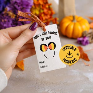 Puede incluir: Una etiqueta de regalo rectangular blanca con una cinta naranja, que presenta el texto negro Happy Halloween at sea! y un gráfico de orejas de ratón con patrones de maíz dulce. La etiqueta incluye líneas para From y Cabin #, más una insignia amarilla.