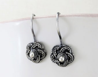 May include: A pair of silver dangle earrings with a floral design. The earrings have a textured, oxidized finish and a small silver bead in the center of each flower.