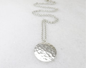 May include: A silver necklace with a hammered round pendant. The chain is a delicate silver chain.