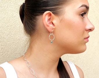 May include: Silver hoop earrings with a small turquoise bead dangling from the bottom.