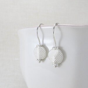 May include: A pair of silver dangle earrings with a textured round disc charm. The earrings have a simple hook closure.