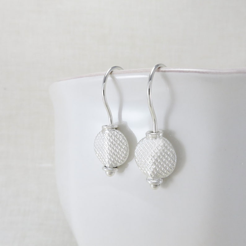 May include: A pair of silver dangle earrings with a textured round disc charm. The earrings have a simple hook closure.