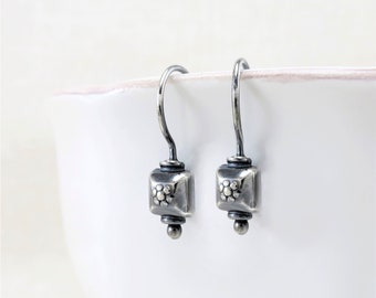 May include: A pair of silver dangle earrings with a square-shaped charm featuring a flower design.