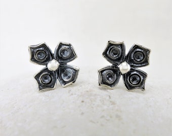May include: A pair of silver flower-shaped stud earrings with a textured finish. Each earring features five rounded petals with a small, round center.