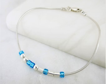 May include: A silver chain anklet with a delicate design and blue glass beads.