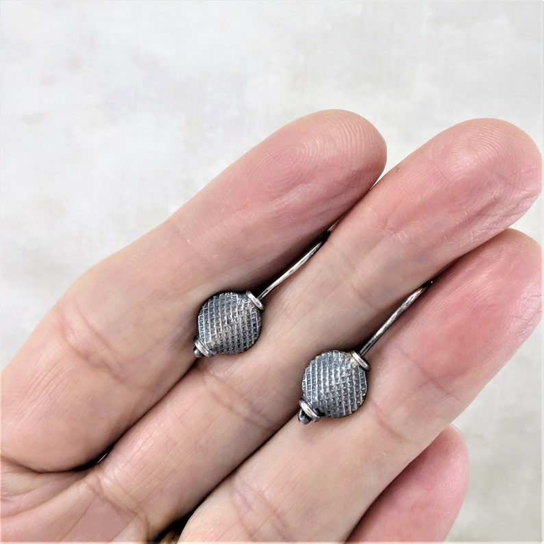 May include: A pair of silver earrings with a textured, round design. The earrings are small and delicate.