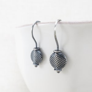 May include: A pair of silver dangle earrings with a textured circular design. The earrings have a simple hook closure.