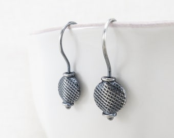 May include: A pair of silver dangle earrings with a textured circular design. The earrings have a simple hook closure.