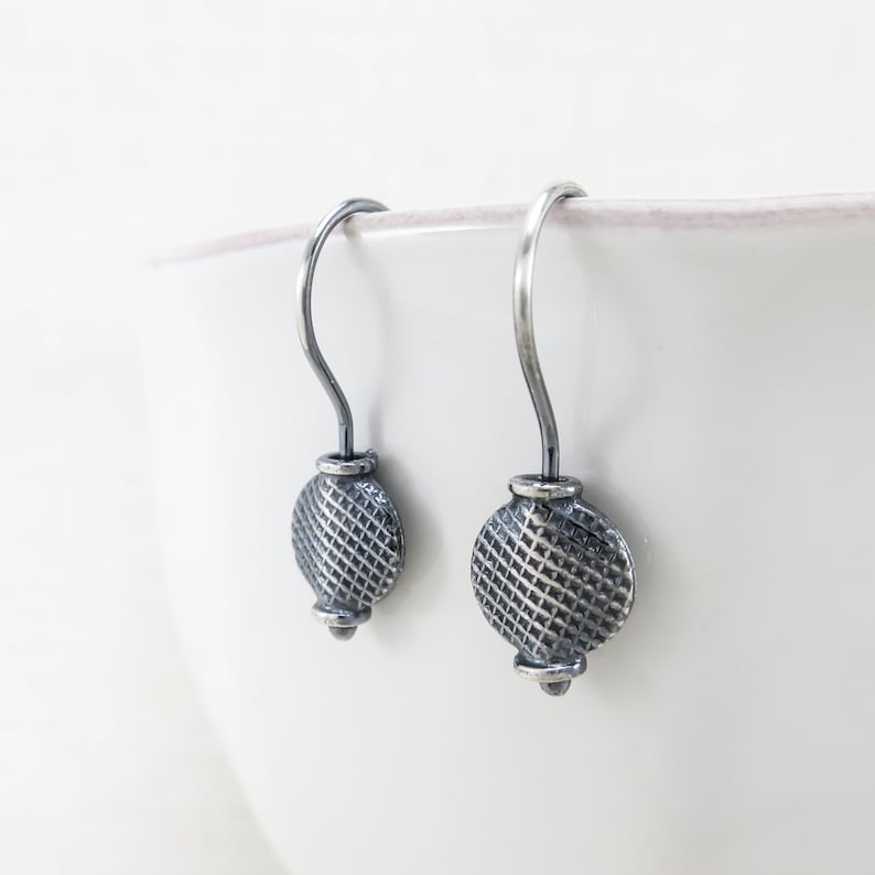 May include: A pair of silver dangle earrings with a textured circular design. The earrings have a simple hook closure.
