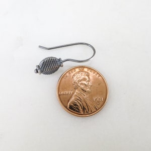 May include: A silver earring with a textured, round design. The earring is shown next to a US penny for size comparison.