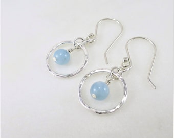 May include: Silver hoop earrings with a light blue gemstone dangling from each hoop.
