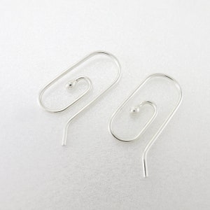 May include: A pair of silver-colored earrings. Each earring features a unique design with a small ball at the top of a spiral shape, connected to a curved hook. The earrings are displayed on a white surface.