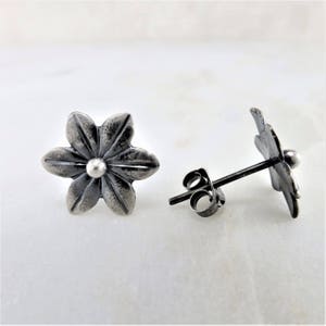 May include: A pair of silver flower stud earrings with a textured finish. The earrings have a small silver bead in the centre of each flower.