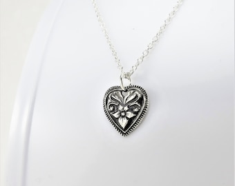 May include: A silver necklace with a heart-shaped pendant featuring an intricate floral design.
