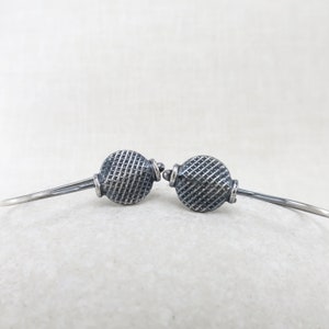 May include: A pair of silver hoop earrings with a textured, circular design. The earrings are oxidized for a darker finish.