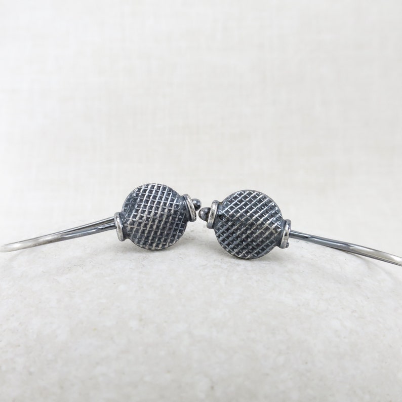 May include: A pair of silver hoop earrings with a textured, circular design. The earrings are oxidized for a darker finish.