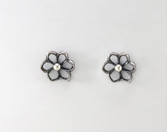 May include: A pair of silver flower stud earrings with a small silver bead in the center of each flower.