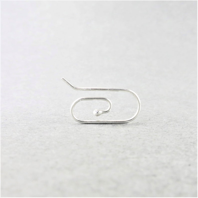 May include: A single, silver-colored earring with a unique, minimalist design. The earring features a curved, open shape with a small, round bead at the center of the spiral. The design is simple and modern, suitable for everyday wear.