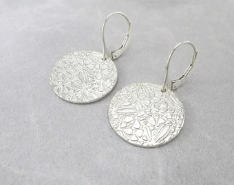 May include: A pair of silver earrings with a circular design. The earrings have a textured surface with a floral pattern.