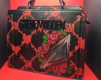 Puede incluir: Bolso de mano de cuero negro con estampado rojo y negro que incluye el texto "Steve Madden" y un gráfico de una máscara con rosas.
