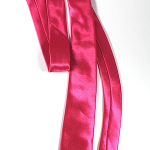 May include: A solid hot pink necktie crafted from a smooth, lustrous satin fabric. The necktie features a classic pointed tip and a long, slender design with a reflective surface that catches the light, showcasing a vibrant and uniform color throughout.
