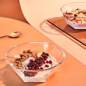 Könnte beinhalten: Zwei Glasschalen gefüllt mit Joghurt, Granola, Obst und Granatapfelkernen. Die Schale links enthält Apfelscheiben, während die Schale rechts eine Auswahl an Früchten enthält.